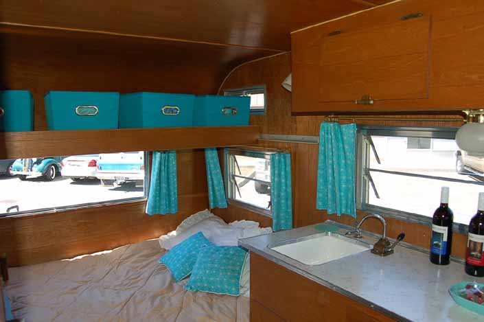 Cozy bed and beautifully re-finished woodwork with overhead storage bins in an Aladdin vintage travel trailer