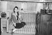Old photo of a woman relaxing on her vintage trailer's couch with her cat, at the Project Hanford Trailer City in Washington