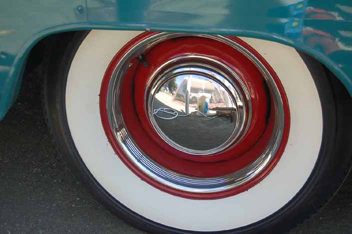 Photo shows an example of a vintage trailer with wheels painted red, with chrome hubcaps beauty rings and wide whitewall tires