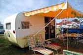 Restored 1958 Aloha travel trailer painted yellow and white with matching yellow chaise lounge chairs