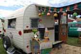 Vintage 1960 Aloha 15-ft trailer and tiki bar with green striped canvas awning and large flower hanging lights