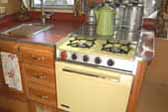 Photo shows restored 1965 Airstream Tradewind trailer with classic yellow gas range and oven