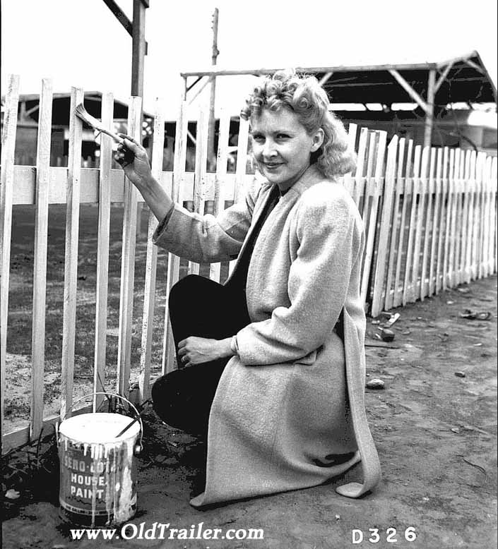 Government photo shows a pretty woman dressed up and painting her picket fence, at the Hanford Trailer Camp in Washington