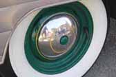 Photo shows a nice example of a vintage trailer wheel painted forest green with a chrome hubcap and wide whitewalls