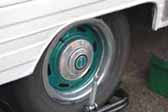 Photo provides a shot of modern wheels painted green, and with a small hubcap, mounted on a vintage travel trailer
