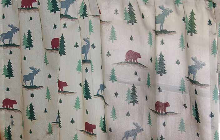 This photo shows a swatch of retro fabric with a moose, bear and pine tree cabin pattern, for your vintage trailer