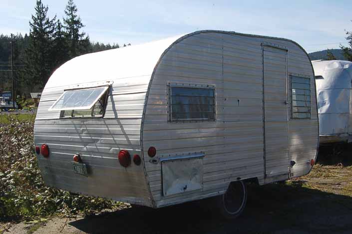 A vintage canned ham trailer with dents in a Vintage Trailer Junk Yard, is a good restoration project candidate