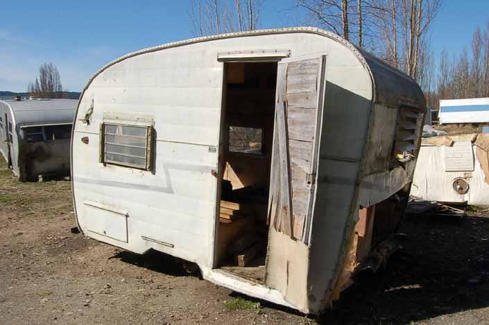 Tired Shasta Compact trailer parked in a vintage trailer StorageYard has its front panel cut away